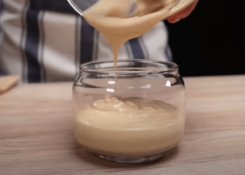 Glazen potje met zelfgemaakte haarboter op een houten tafel, omringd door verse rozemarijn, kruidnagels en flesjes met natuurlijke oliën – symbool voor natuurlijke haarverzorging en haargroei.