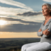 Een vrouw van rond de 45 tot 55 jaar oud staat op een klif of heuveltop bij zonsopgang of zonsondergang. Ze kijkt zelfverzekerd en vredig uit over een wijde, open horizon – symbool voor nieuwe levensfasen, innerlijke kracht en vrijheid. Ze draagt comfortabele, stijlvolle kleding, haar houding is open, haar gezicht straalt rust en vastberadenheid uit. De natuur om haar heen straalt kalmte en schoonheid uit – perfect voor het gevoel van “nieuw begin” en persoonlijke groei.